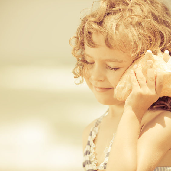 Happy child listen to seashell at the beach. Summer vacations concept