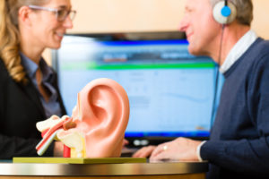 Older man or pensioner with a hearing problem make a hearing test and may need a hearing aid, in the foreground is a model of a human ear